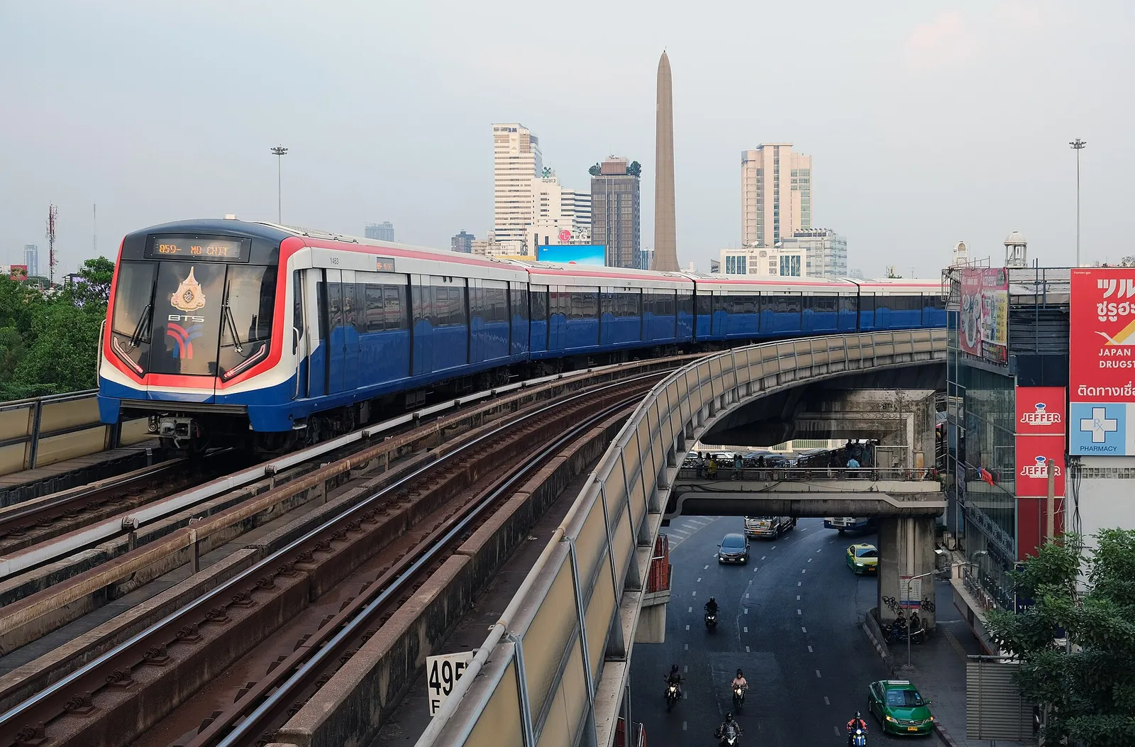 רכבת ה-BTS סקיי טריין חולפת מעל רחוב סואן עם שלטי ניאון בבנגקוק תאילנד בשעת ערב