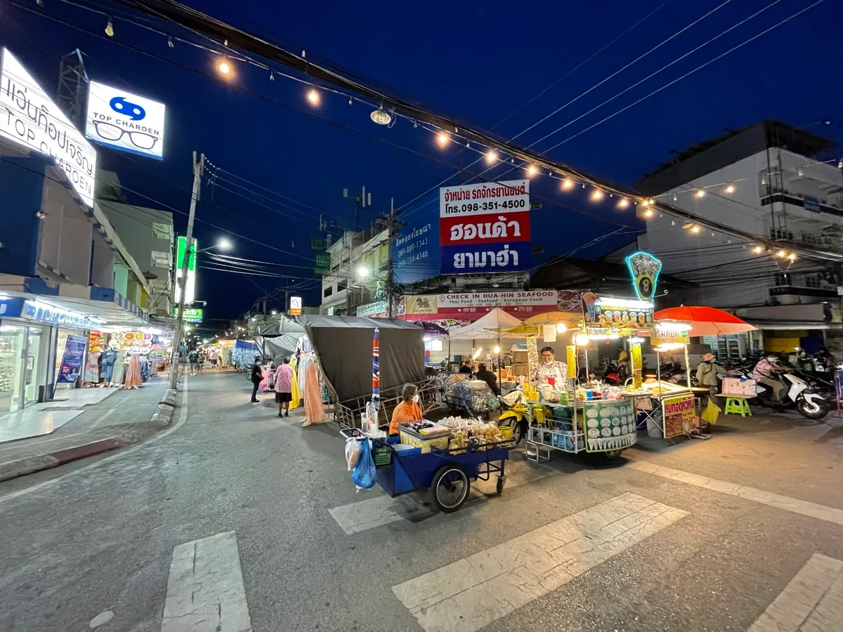 רחוב שוק בערב עם שרשראות נורות, דוכני אוכל ניידים ושלטים מוארים