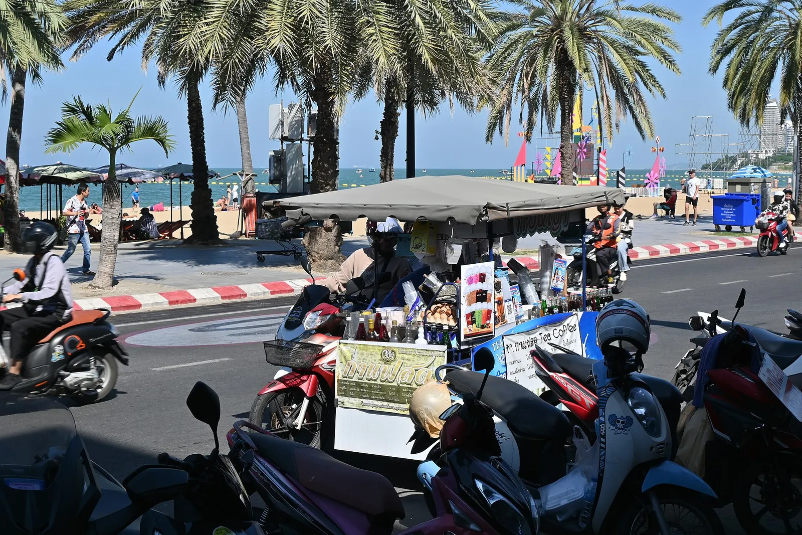 קטנועים חונים לצד רחוב חוף בפאטאיה תאילנד עם קסדה על הכידון ורוכב חובש קסדה ברקע